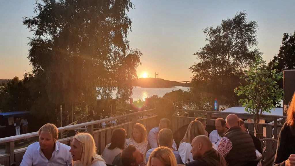 Solnedgång över Surfvikens uteservering som blickar ut över Tjörnbron, Glada gäster som njuter av sommarvärmen.