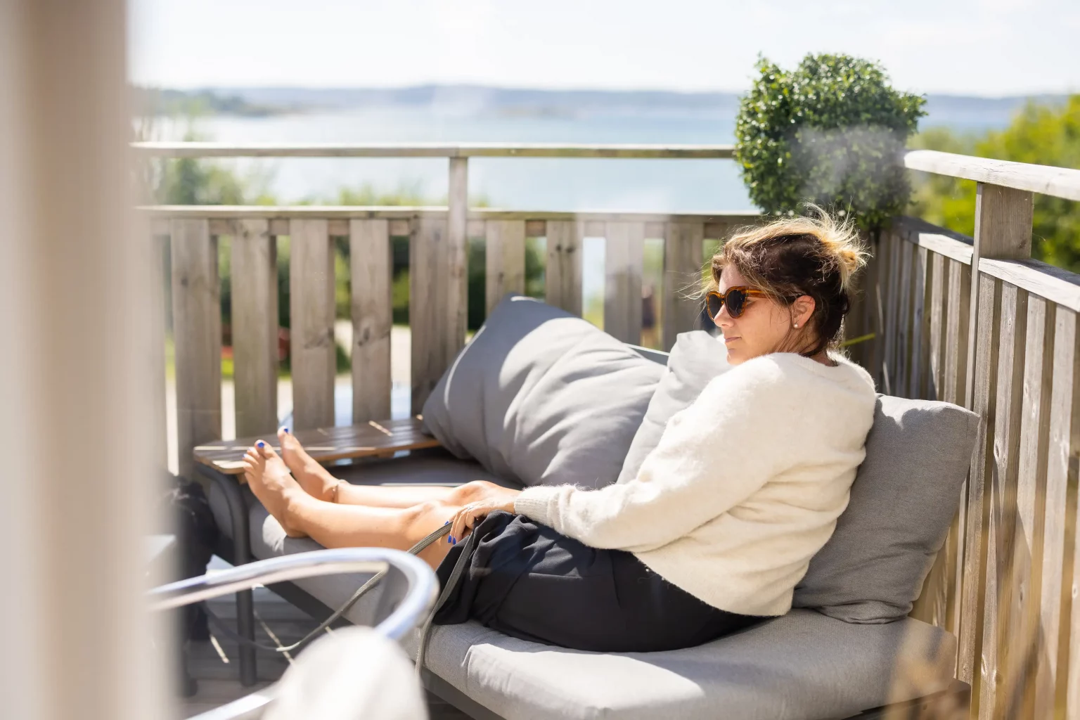 En tjej som sitter och njuter av vårsolen i soffan på vår uteservering med havet som närmsta granne.