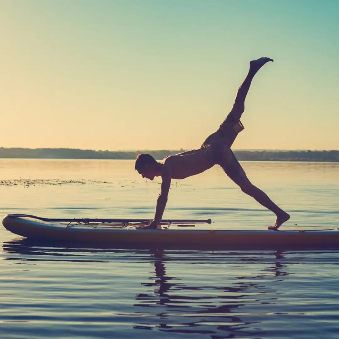 En kille som gör SUP yoga i solnedgången