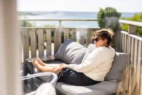 En tjej som sitter och njuter av vårsolen i soffan på vår uteservering med havet som närmsta granne.